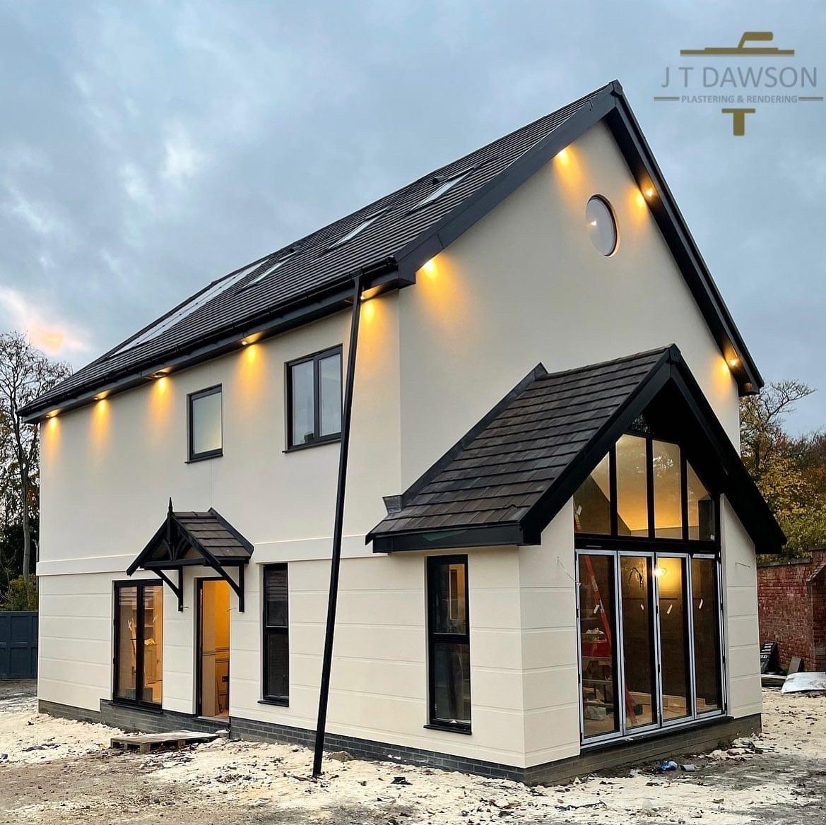 New-build house finished in cream render, soffit lights on at dusk, by J T Dawson