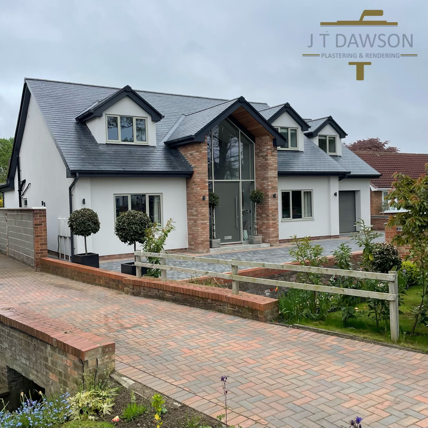 Detached house finished in white render with a brick feature gable, by J T Dawson