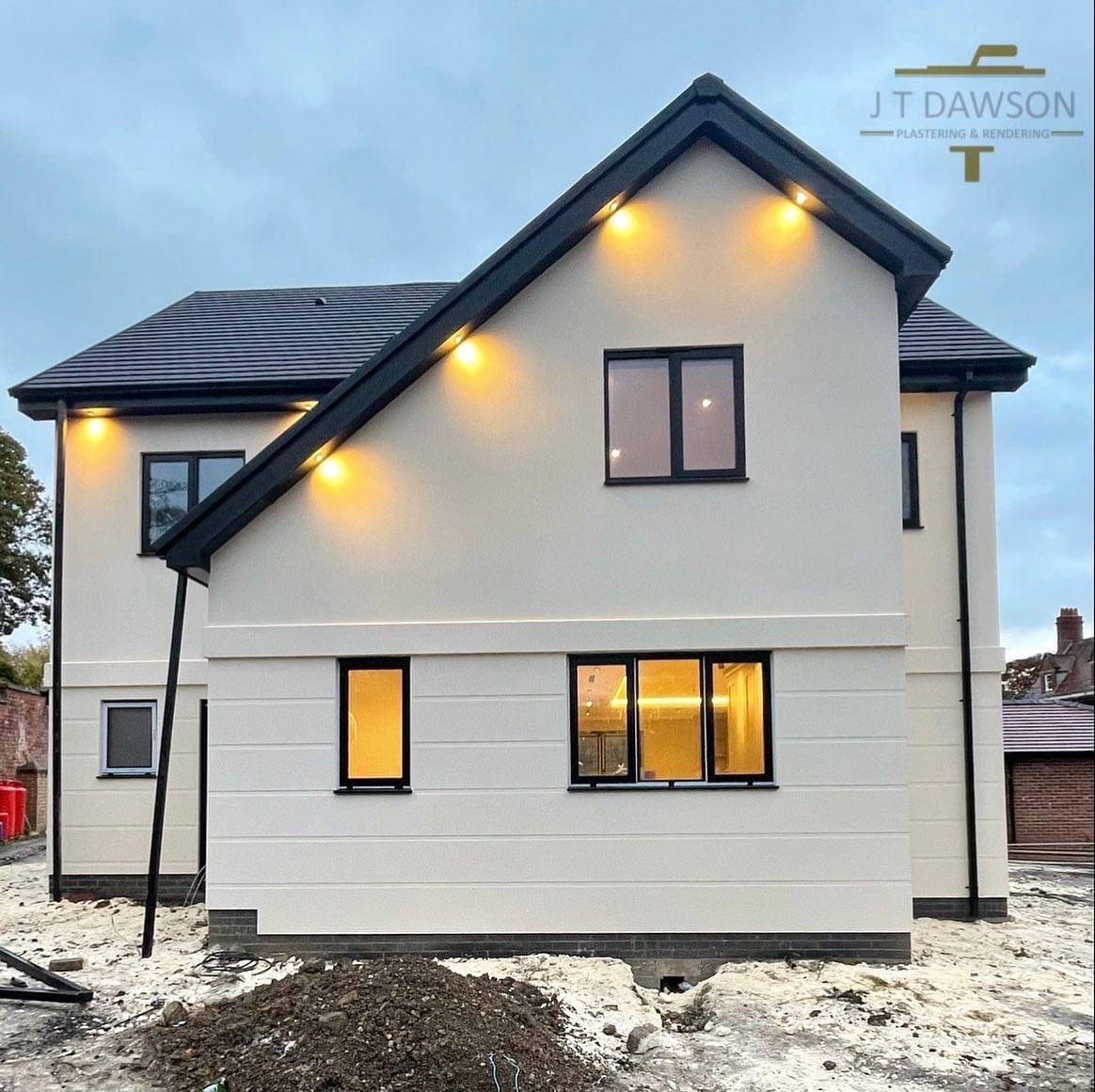 New-build house in cream render at dusk with lit soffits, by J T Dawson