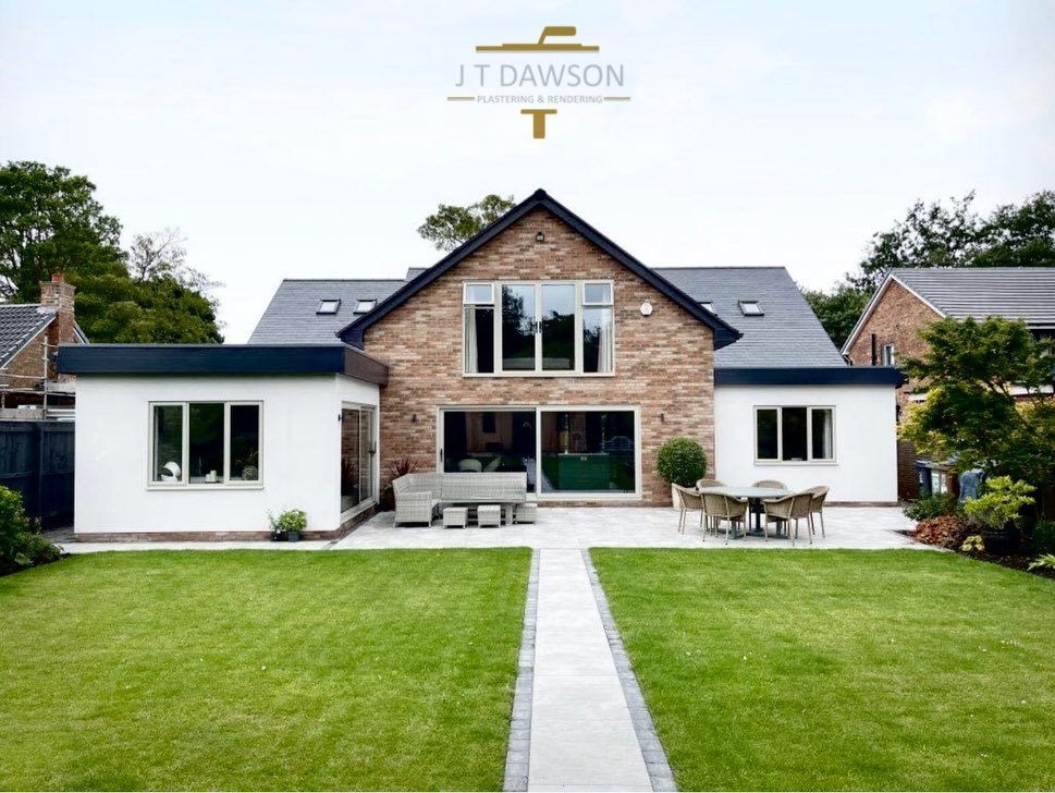 Rear of a house with a white-rendered single-storey extension and lawn, by J T Dawson