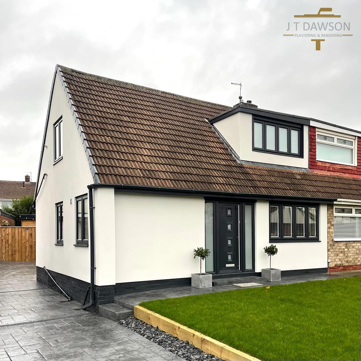 Semi-detached house in white render with a black plinth, by J T Dawson